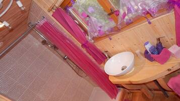 A wooden cabin bathroom with a shower, a sink, and a window with a view of flowers.