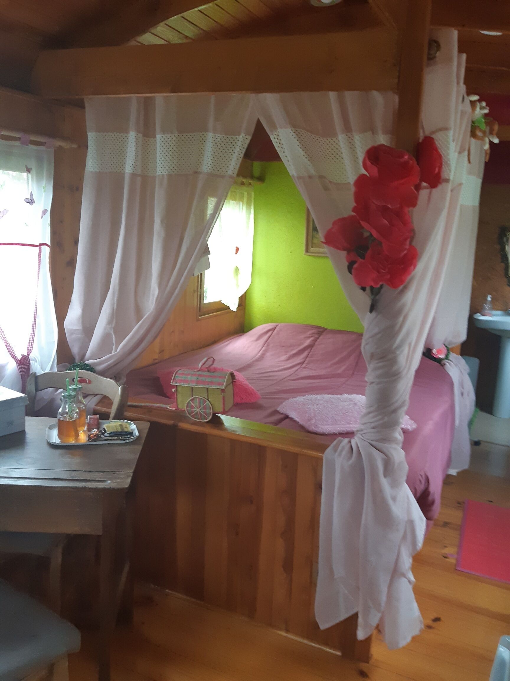Una habitación acogedora con una cama bajo un dosel, una mesita con una bandeja y una ventana con cortinas.