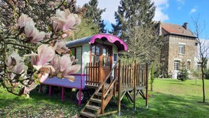 A wooden playhouse with a purple roof and a staircase leading up to it, surrounded by a grassy area with fallen leaves. - Roulotte la Verdine (Dury)