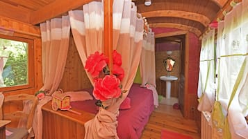 A cozy wooden cabin bedroom with a canopy bed, a small wooden chair, a nightstand, and a window with curtains.