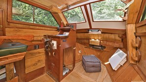 A compact cabin with wooden walls and a sloped roof, featuring a small kitchenette, a wooden desk, and a large window offering a view of the forest. - Roulotte la Verdine (Dury)