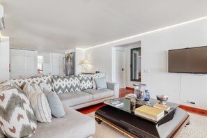 A modern living room with a sectional sofa, a coffee table, and a flat-screen TV mounted on the wall. - GARDEN MARINA APARTMENT (Vilamoura)