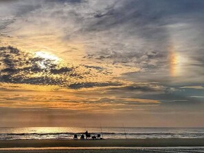 Eine Strandlandschaft bei Sonnenuntergang, mit einigen Personen und einem Boot.