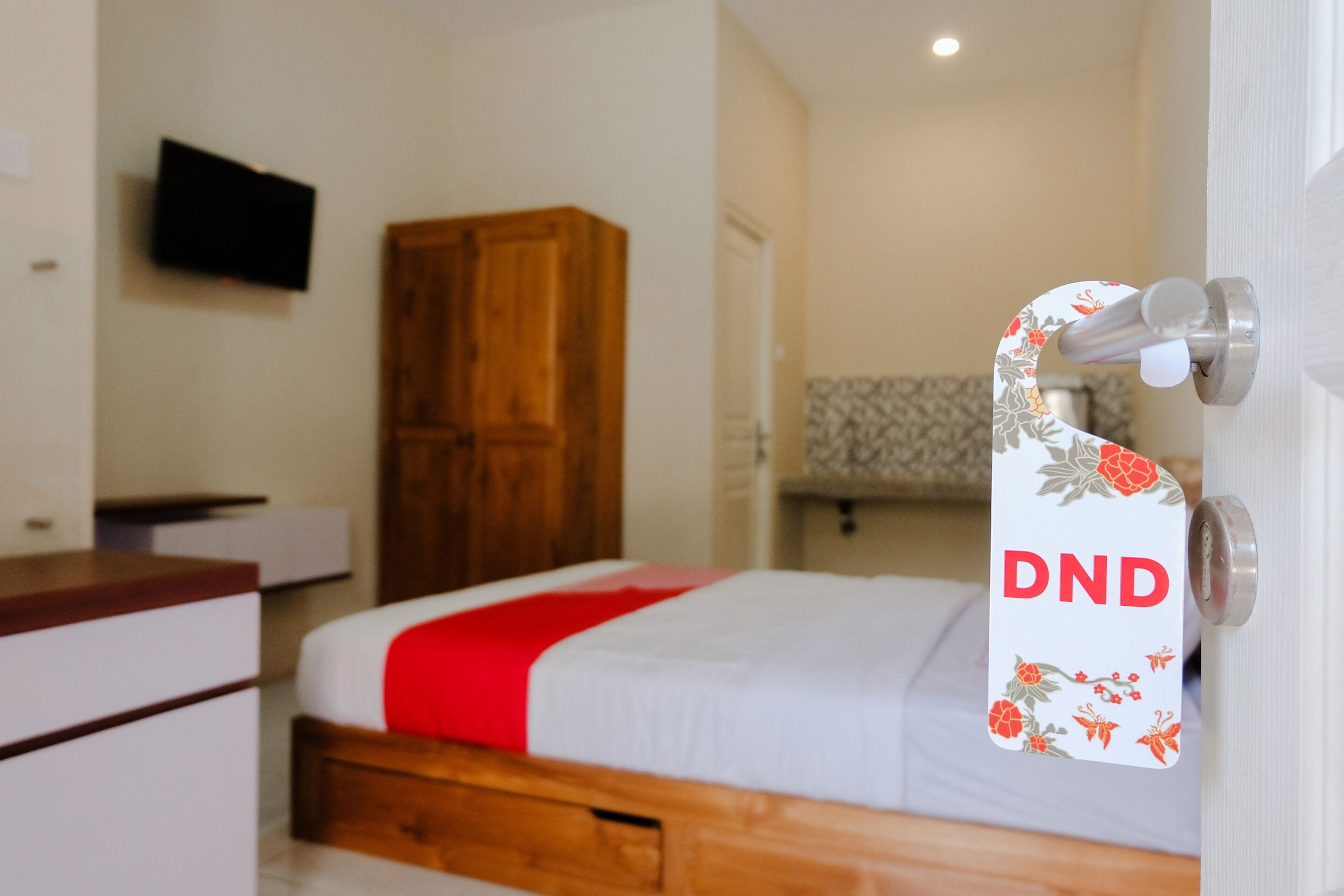Habitació d'hotel amb un llit, un armari de fusta i una televisió penjada a la paret.