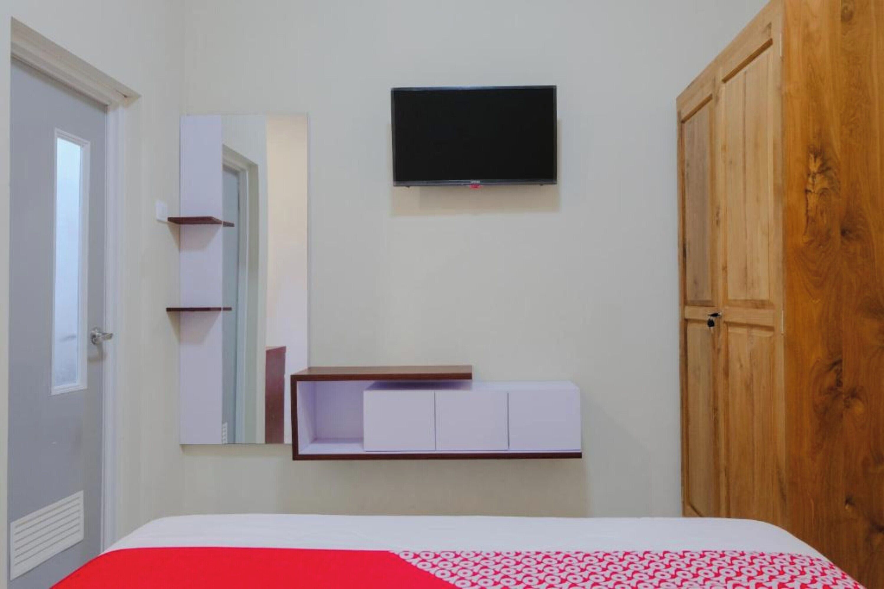 Un dormitorio con cama, televisión montada en la pared, armario de madera y espejo.