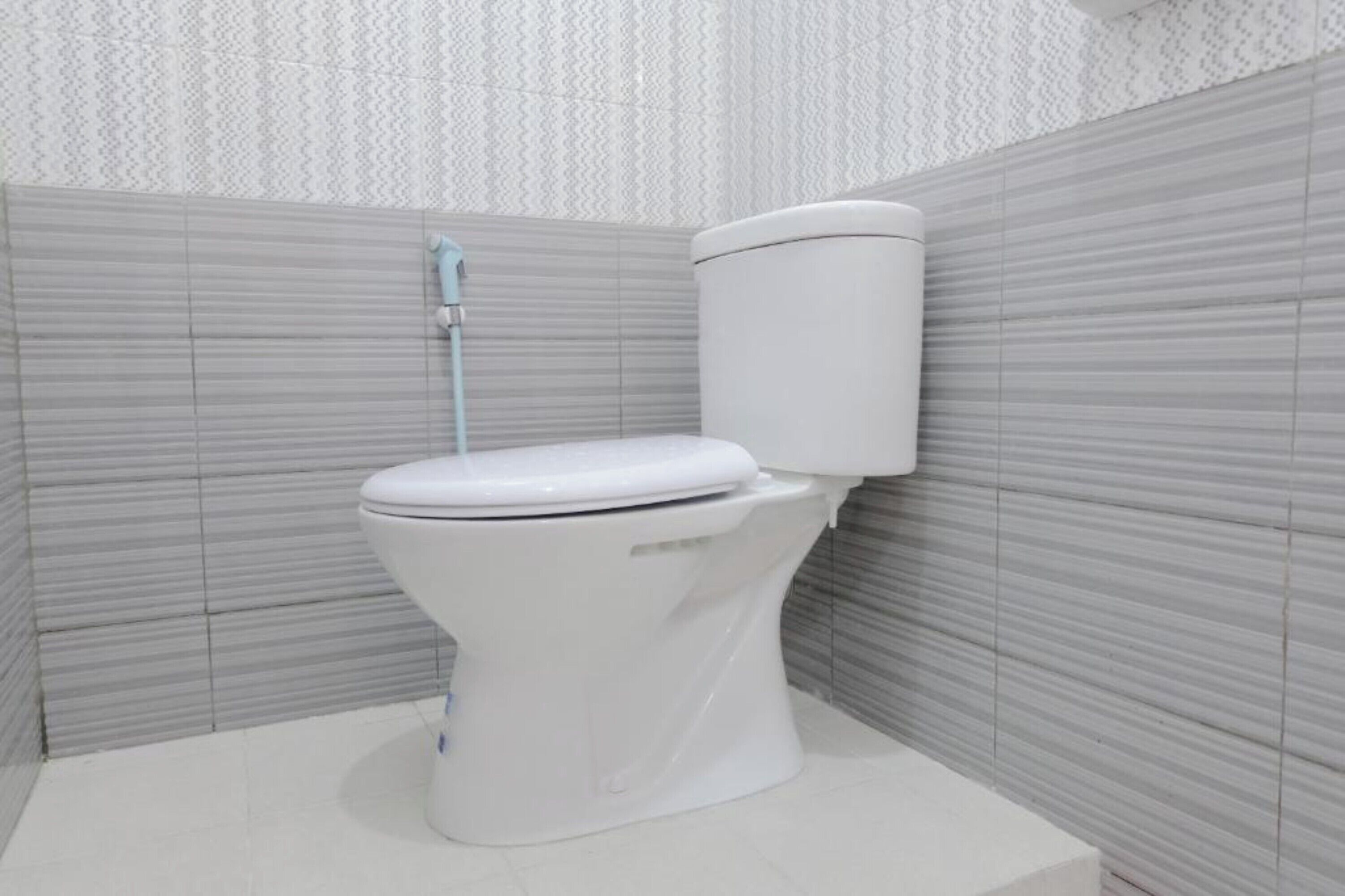 Et hvidt toilet med tanke og sæde i et badeværelse med mønstrede grå fliser.