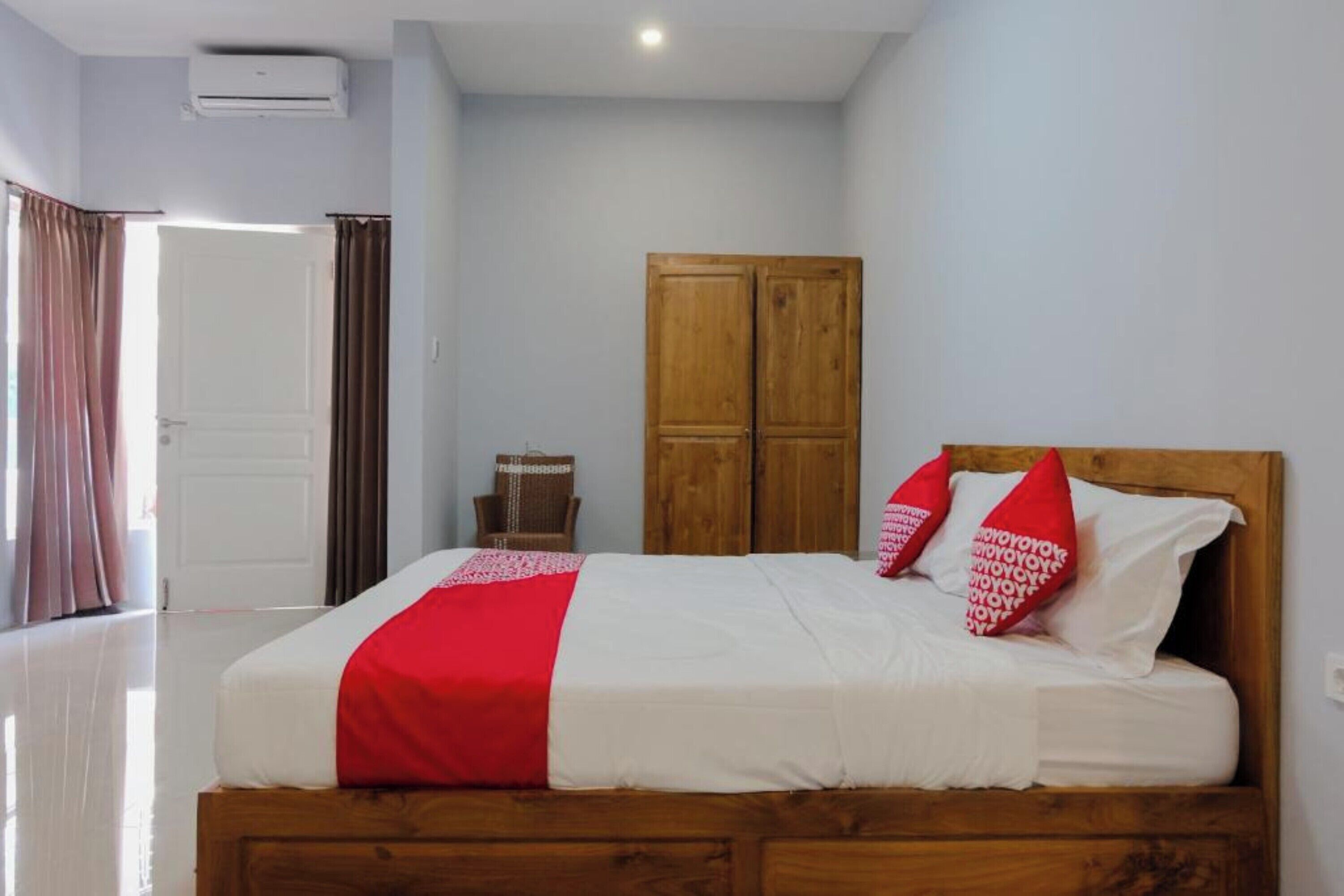 Un dormitorio con cama de madera, ropa de cama blanca y almohadas rojas.