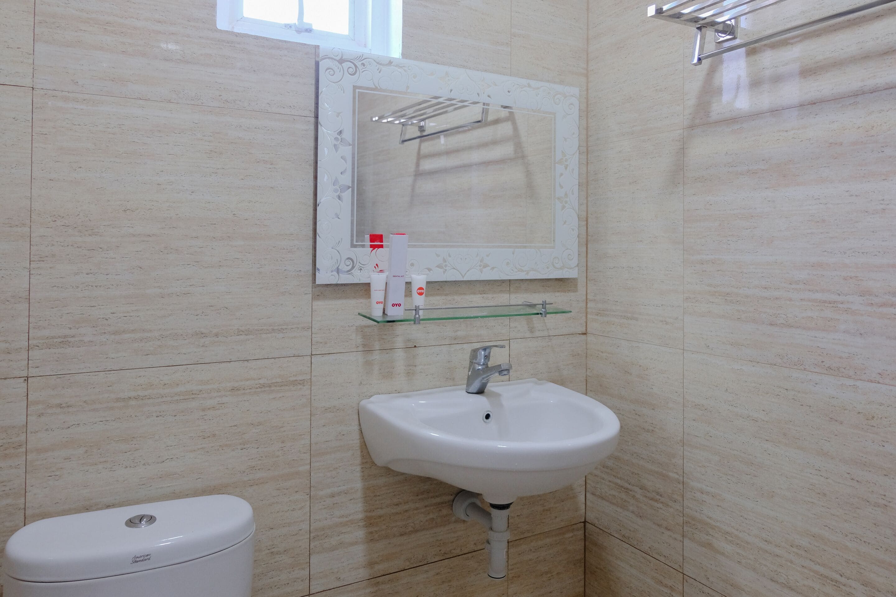 Une salle de bain avec un lavabo blanc, un miroir doté d’un cadre décoratif et une étagère en verre au-dessus du lavabo.