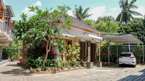 Une maison moderne dotée d’une allée couverte, entourée d’une végétation luxuriante et de palmiers.