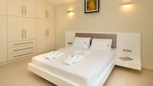 A modern bedroom with a large bed, white linens, a headboard, and a wardrobe with multiple compartments. - Villa Alba (Hersonissos)
