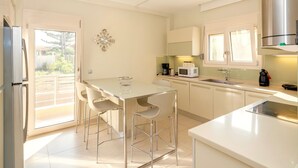 A modern kitchen with a central island, stainless steel appliances, and a large window providing natural light. - Villa Alba (Hersonissos)