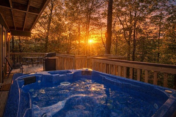 A hot tub on a wooden deck with a view of trees and a sunset. - Happy Trails- easy access, 3 minute drive to Pigeon Forge (Pigeon Forge)