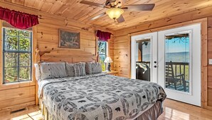 A wooden cabin bedroom with a bed, a ceiling fan, and a window with a view of the outdoors. - Smoky Mountain Views  - AWESOME MOUNTAIN VIEWS, $560 FREE tickets each paid day (Sevierville)