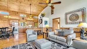 A spacious living area with a sofa, ottoman, and a dining table with chairs. A kitchen with wooden cabinets and a microwave is visible in the background. - Smoky Mountain Views  - AWESOME MOUNTAIN VIEWS, $560 FREE tickets each paid day (Sevierville)
