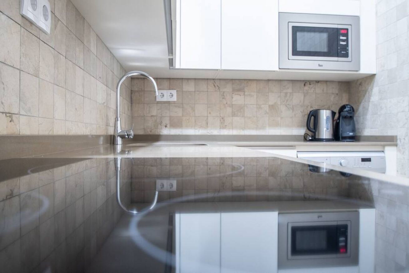 A modern kitchen with a reflective countertop, a built-in microwave, and a coffee maker.