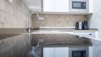 A modern kitchen with a reflective countertop, a built-in microwave, and a coffee maker.
