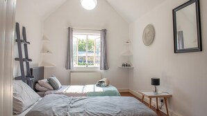 Une chambre avec deux lits, un puits de lumière, une fenêtre avec des rideaux, une table de chevet avec une lampe et un miroir fixé au mur.