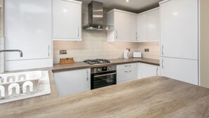 Une cuisine moderne avec des armoires blanches, une hotte en acier inoxydable, un four encastré et un plan de travail en bois.