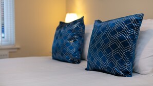 Un lit avec une literie blanche et deux oreillers bleus ornés d’un motif géométrique.