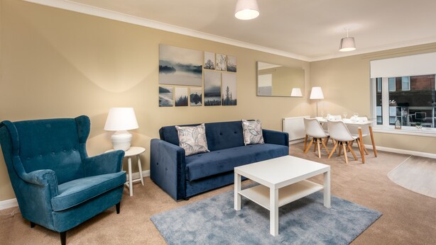 Un salon avec un fauteuil bleu, un canapé bleu foncé, une table basse blanche et un coin repas avec une petite table et des chaises.