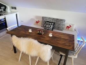A dining area with a wooden table, white chairs, and a fluffy white chair. There are decorative pillows with animal prints and a sign that says "I LOVE SO MUCH I COULD".