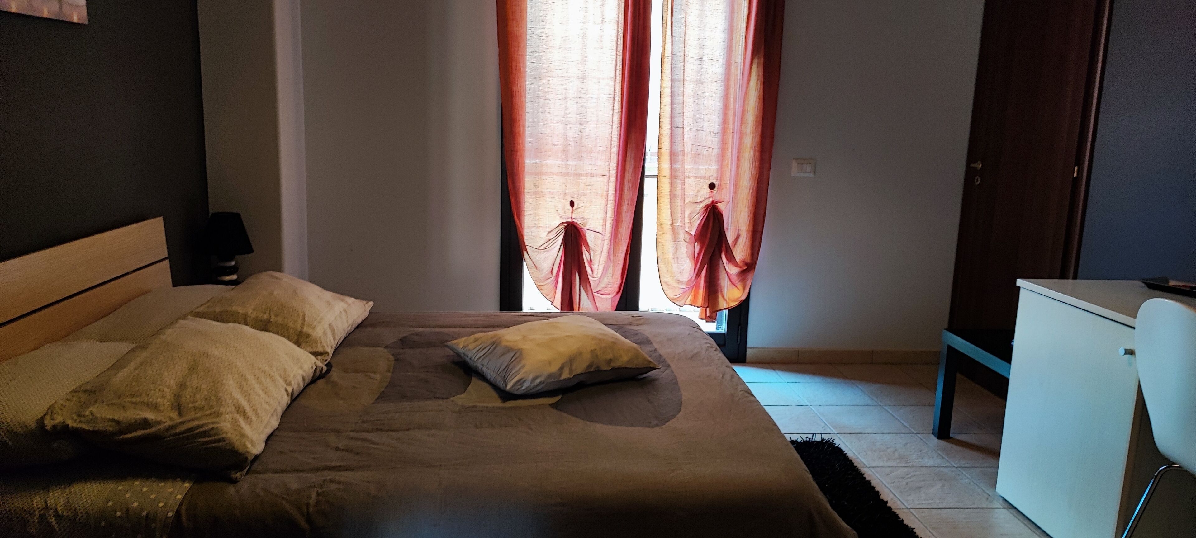 Une chambre à coucher avec un lit, des oreillers, un bureau et des rideaux.