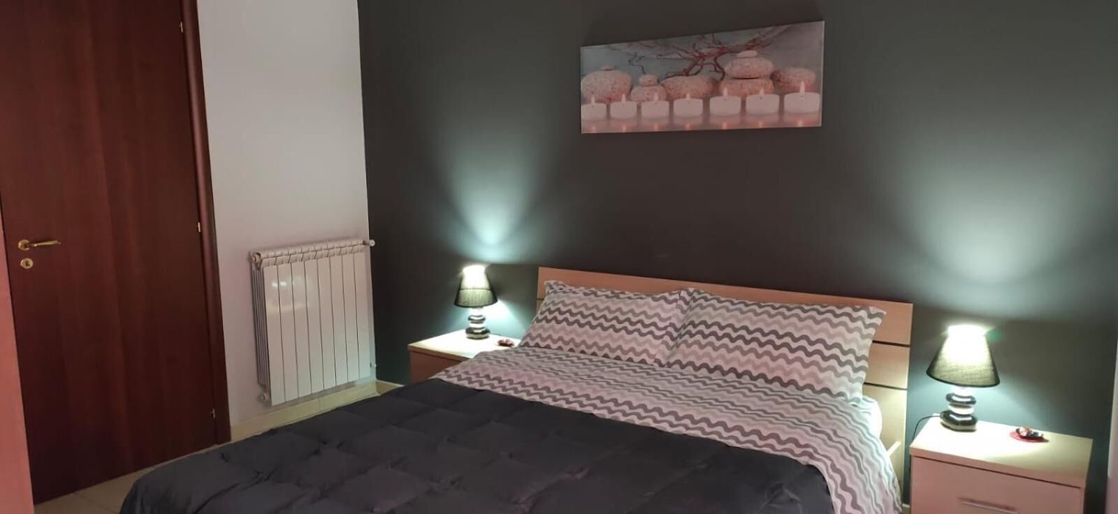 A bedroom with a bed, two bedside tables with lamps, a radiator, and a door.