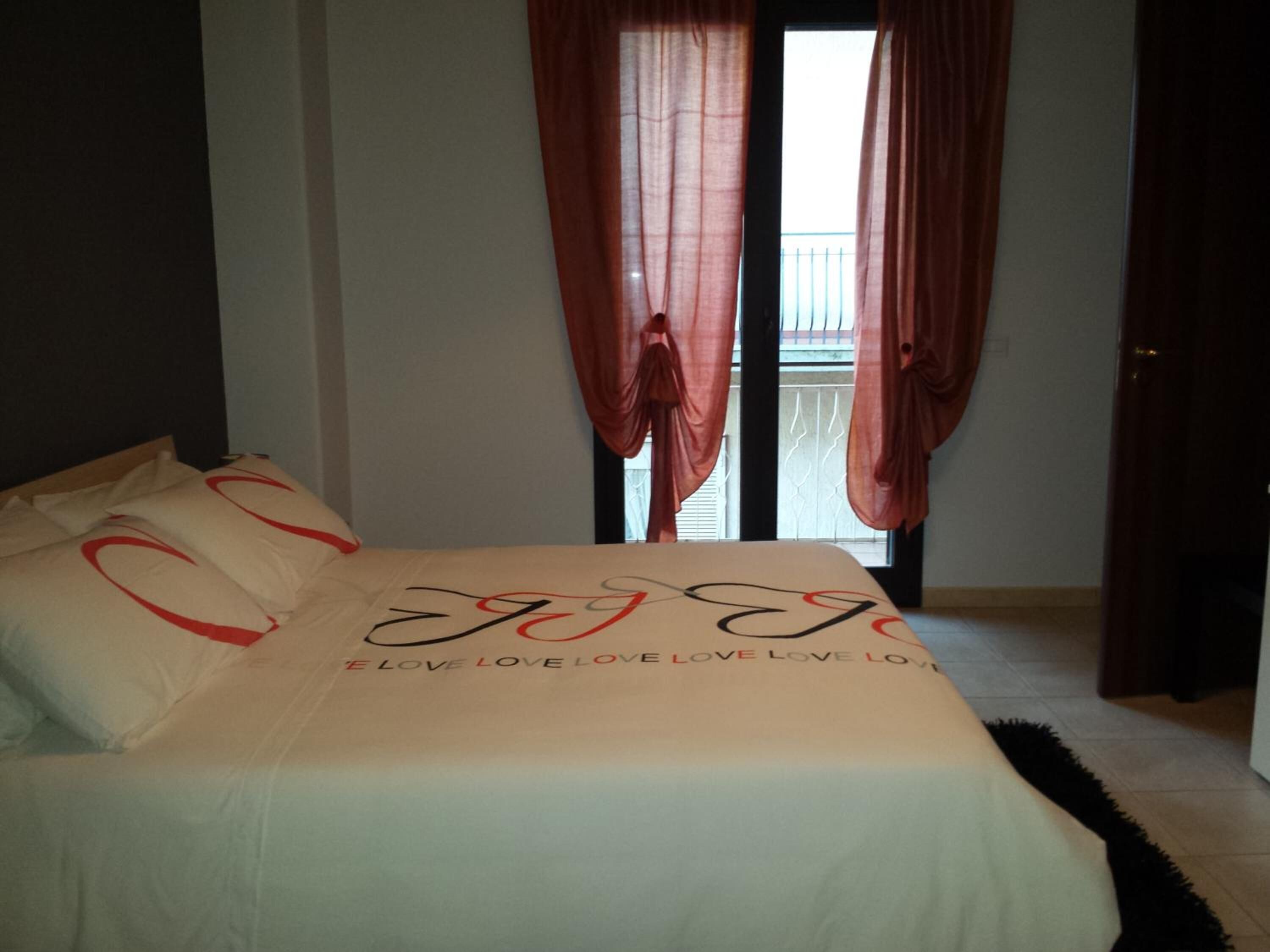 A bedroom with a bed, red curtains, and a view of the outside.