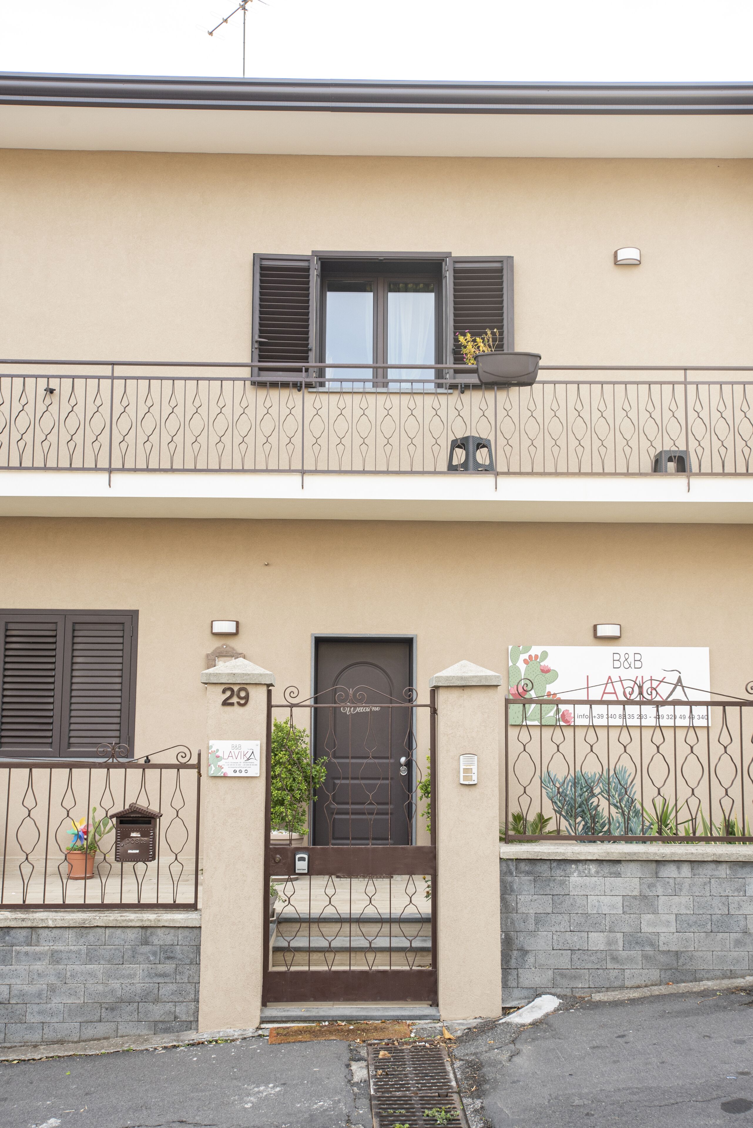 Un edificio a due piani con un balcone, una porta con una targa e un cancello.