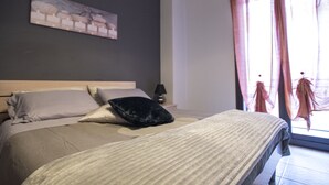 A bedroom with a bed, pillows, a nightstand, a lamp, and a window with curtains. - B&B Lavika Pedara (Pedara)