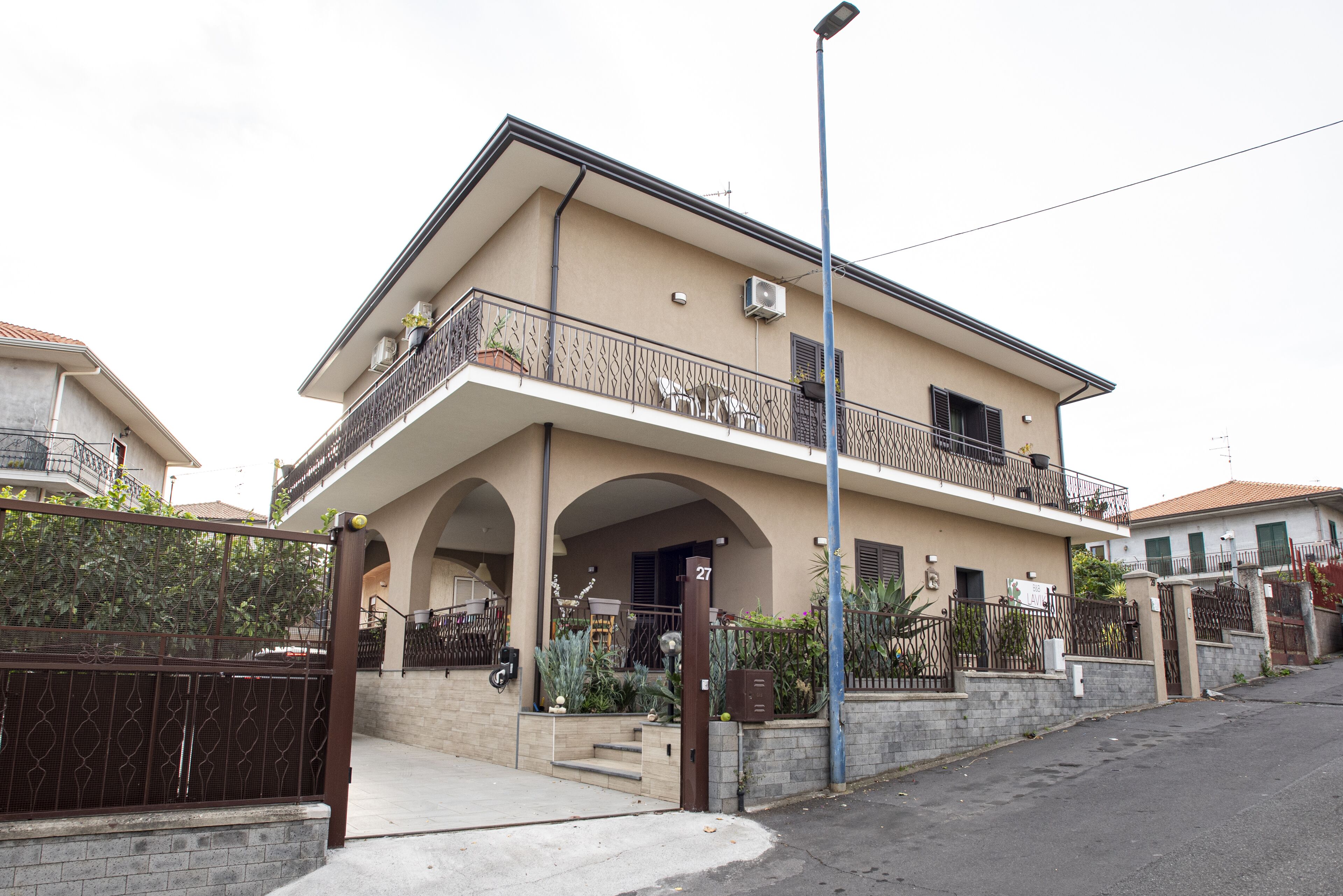 A two-story residential building with a balcony, a gated entrance, and a visible number 27.