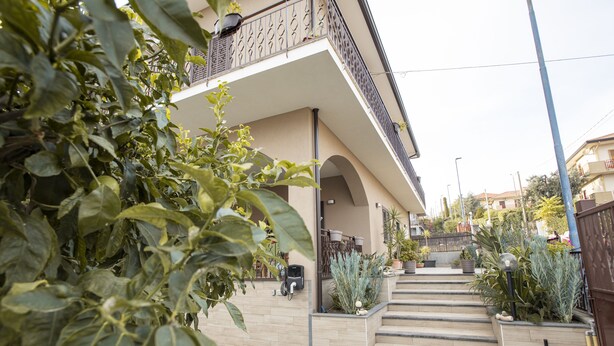 A building with a staircase leading to a balcony, surrounded by potted plants and a clear sky. - B&B Lavika Pedara (Pedara)