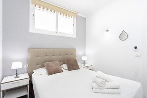 Une chambre d’hôtel avec un lit, deux tables de chevet, une fenêtre avec des stores, un luminaire fixé au mur et une serviette sur le lit.