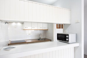 Una cocina compacta con armarios blancos, microondas integrado y encimera de madera.
