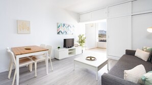 A modern living room with a dining area, a flat-screen TV, a potted plant, and a view through a sliding door. - Encantador apto. Vistas al mar.WIFI (Callao Salvaje)