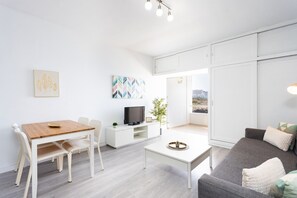 Una sala moderna con comedor, televisor de pantalla plana, planta en maceta y vistas a través de una puerta corredera.