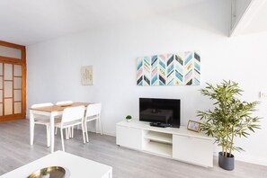 Un salon moderne comprenant un coin repas, un téléviseur à écran plat posé sur un meuble blanc et une plante en pot.