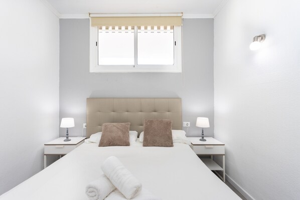 A hotel room with a bed, two nightstands, two lamps, a window with a blind, and a towel on the bed.