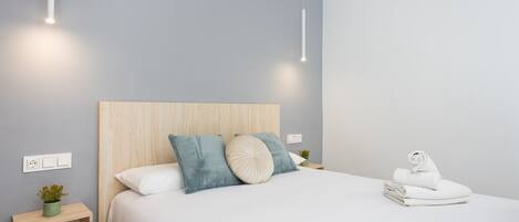 A modern bedroom with a wooden headboard, a neatly made bed with white linens, and a small bedside table with a plant.