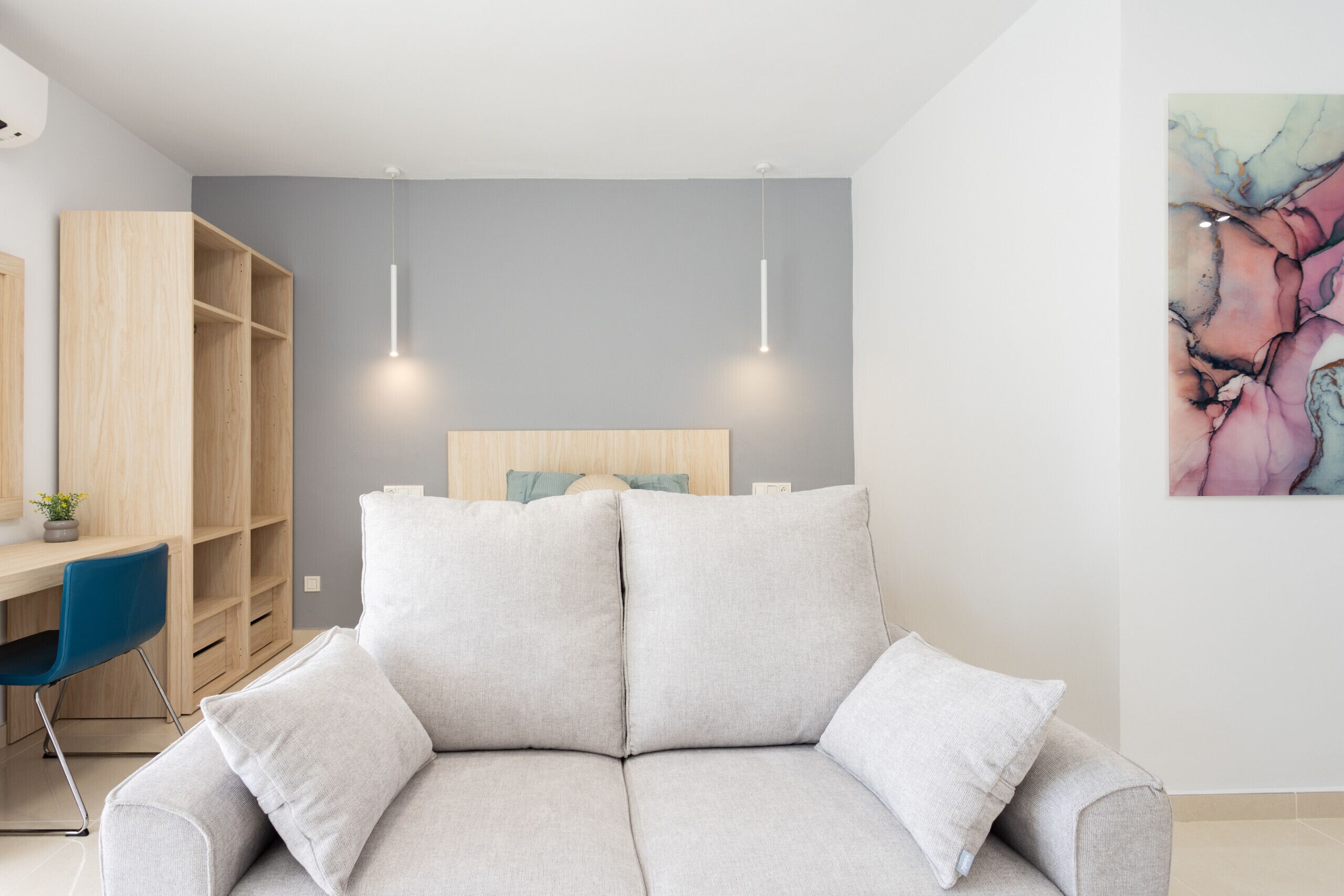 A modern living room with a grey sofa, a wooden desk, and a blue chair.
