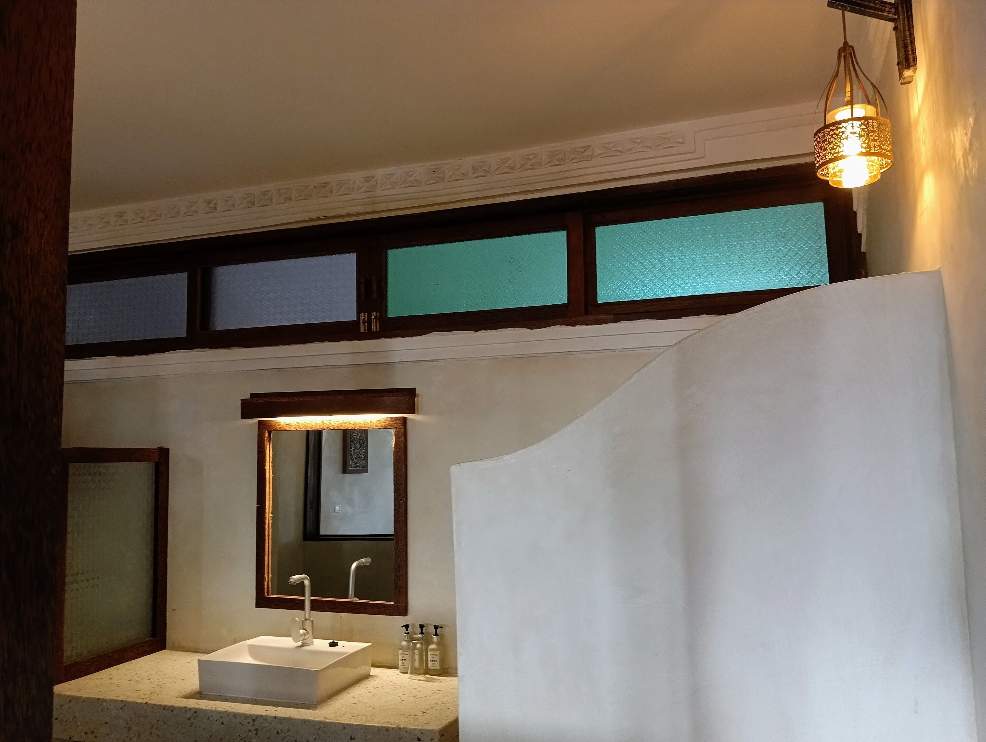 Un baño con lavamanos blanco, un espejo y una lámpara colgante.