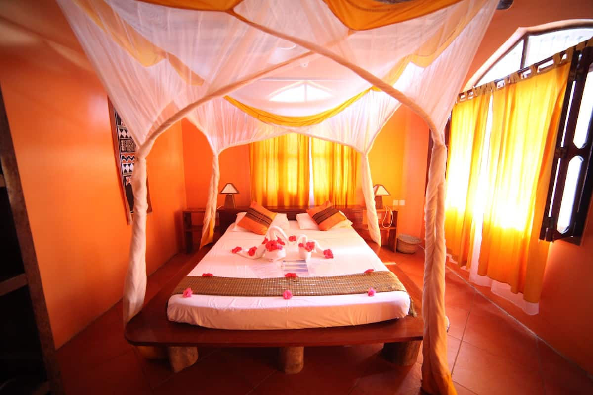 A room with a bed under a canopy, a nightstand, a lamp, and a window with curtains.