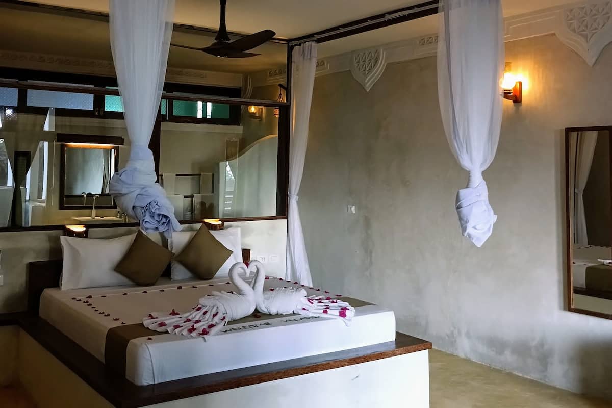 A bedroom with a canopy bed, a ceiling fan, and a wall-mounted light fixture.