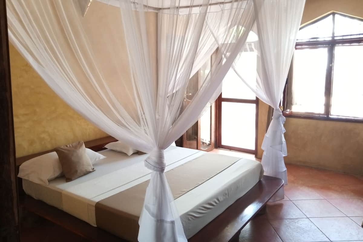 A room with a bed under a white canopy, a window with a view, and a tiled floor.