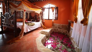 Une chambre avec un lit, une baignoire en pierre et une fenêtre avec des rideaux.