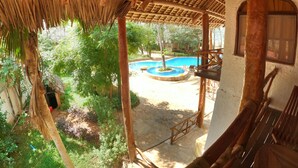 Une construction à toit de chaume, dotée d’une piscine et entourée d’une végétation luxuriante.