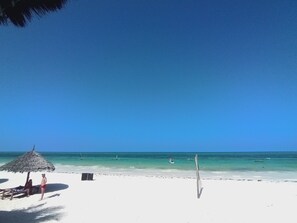 A beach with a thatched umbrella, a wooden chair, and a wooden post. - Villa Dida Resort (Pwani Mchangani)