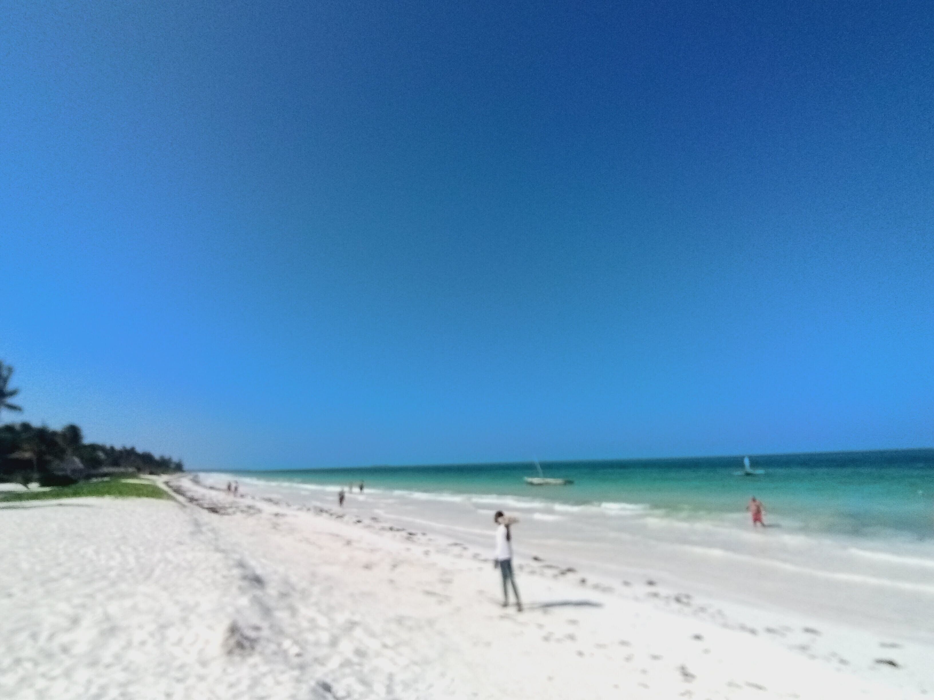 A beach with a clear sky, sandy shore, and a few people walking.
