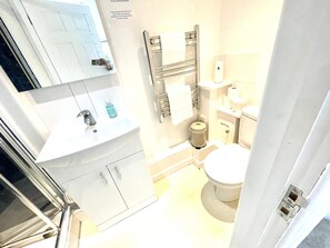 A compact bathroom with a white sink, mirror, and toilet. There are toiletries and a towel rack visible. - Mill Apartment (Cambridge)
