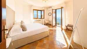A bedroom with a bed, a desk, a chair, and a balcony with a view. - AMORE RENTALS - Villa Raffaella with Private Pool and Sea View (Sant´Agata sui Due Golfi)